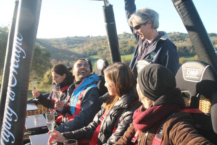 Group of people drinking in a hot air balloon basket over a scenic landscape.