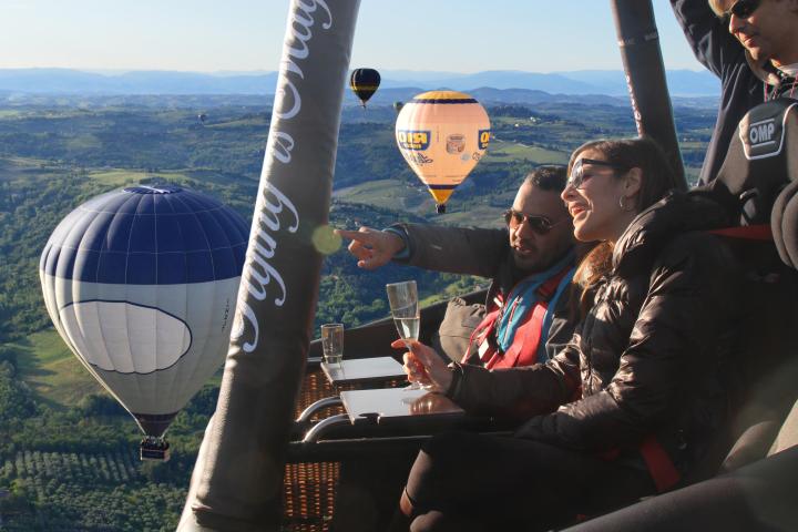 People in a hot air balloon, enjoying a scenic view with other balloons in the background.