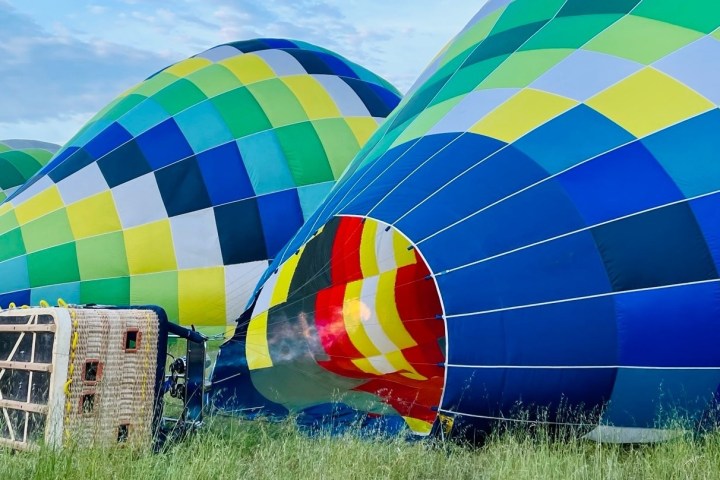 Colorful hot air balloons inflating on grass field with basket nearby.