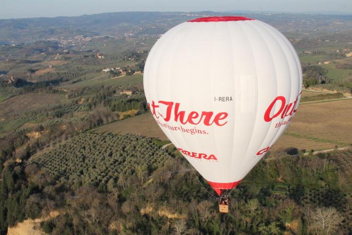 White hot air balloon over green and brown landscape with hills in the background.